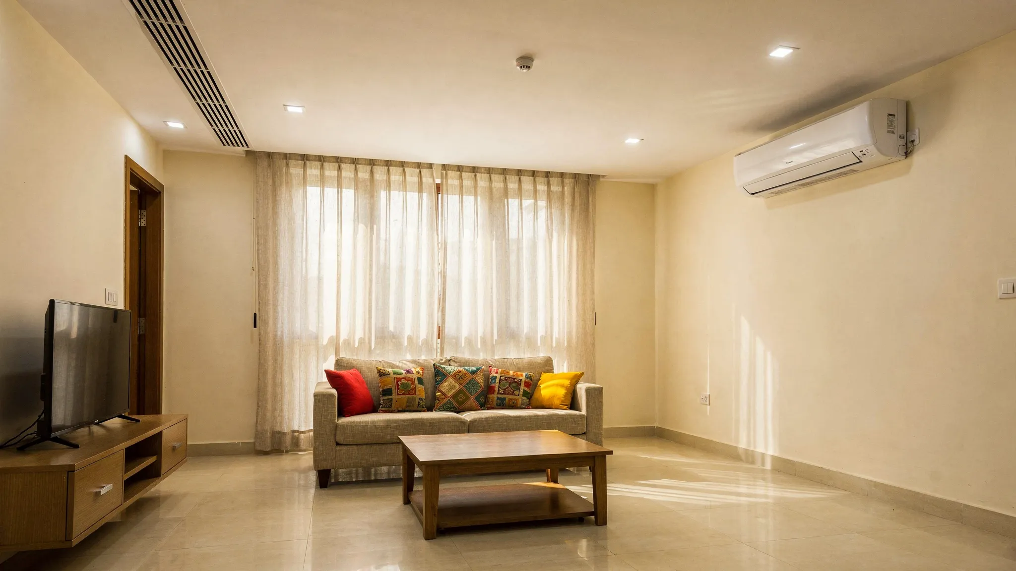 A modern Chennai apartment living room with a concealed ductable AC diffuser in the false ceiling on one side and a wall mounted split AC indoor unit shown on the other side for comparison.