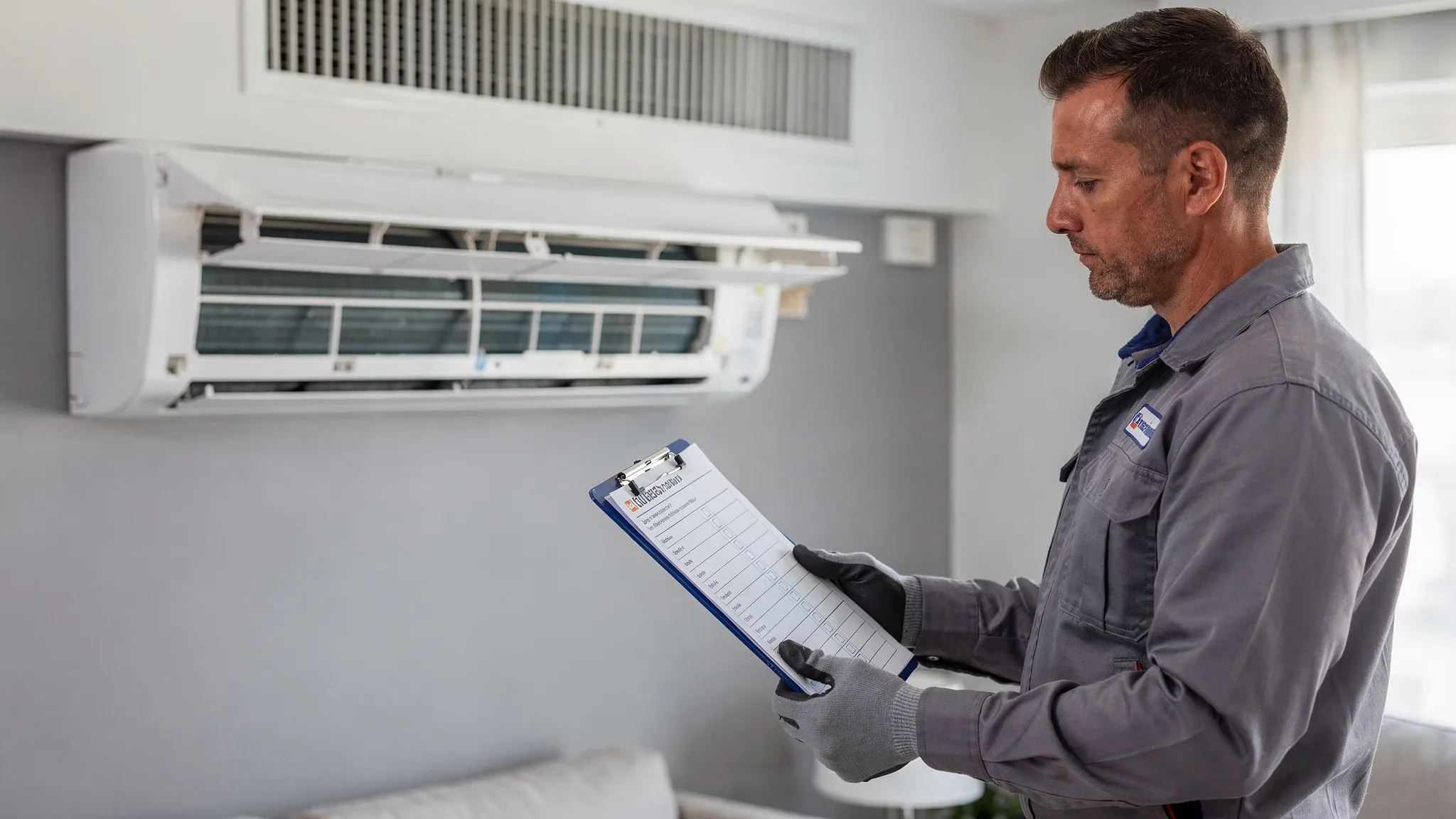 A technician performing a professional AC inspection showing a checklist clipboard beside a clean indoor unit filter and a centralised duct vent, representing preventive maintenance and energy efficiency checks for both system types.